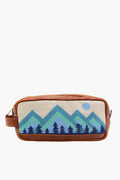 A rectangular brown Italian leather toiletry bag by Smathers and Branson, featuring a fabric front panel with hand-stitched needlepoint of blue and green mountains, forest, and a blue sun.