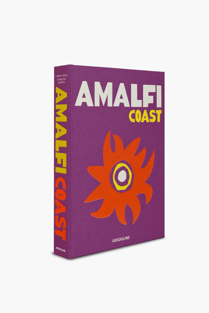 The Assouline hardcover book "Amalfi Coast" features a vivid purple cover, bold yellow and white lettering, and an abstract orange flower—reflecting the lively spirit of Italian travel along the Mediterranean Sea.