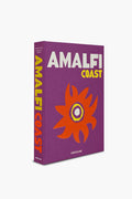 The Assouline hardcover book "Amalfi Coast" features a vivid purple cover, bold yellow and white lettering, and an abstract orange flower—reflecting the lively spirit of Italian travel along the Mediterranean Sea.