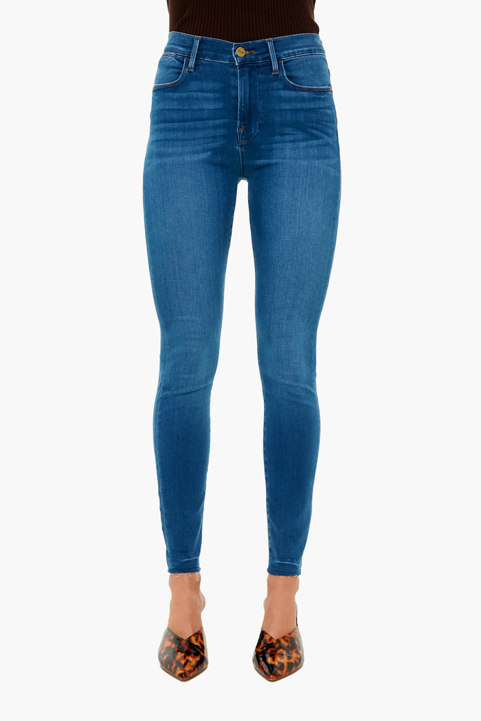 A person wearing FRAME blue high rise skinny jeans crafted from sustainable denim, paired with brown animal print pointed-toe shoes.