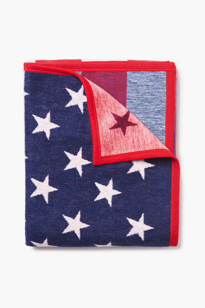 The ChappyWrap folded American flag blanket features white stars, red trim, and a peek of its red stripe and star pattern inside, adding a cozy and durable touch to your home.