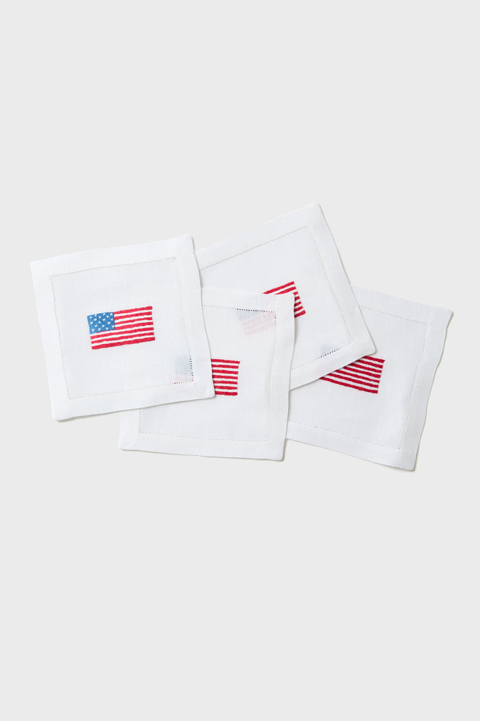 Set of four white linen cocktail napkins by Tuckernuck Home, each with a small embroidered American flag in one corner—makes a thoughtful hostess gift.