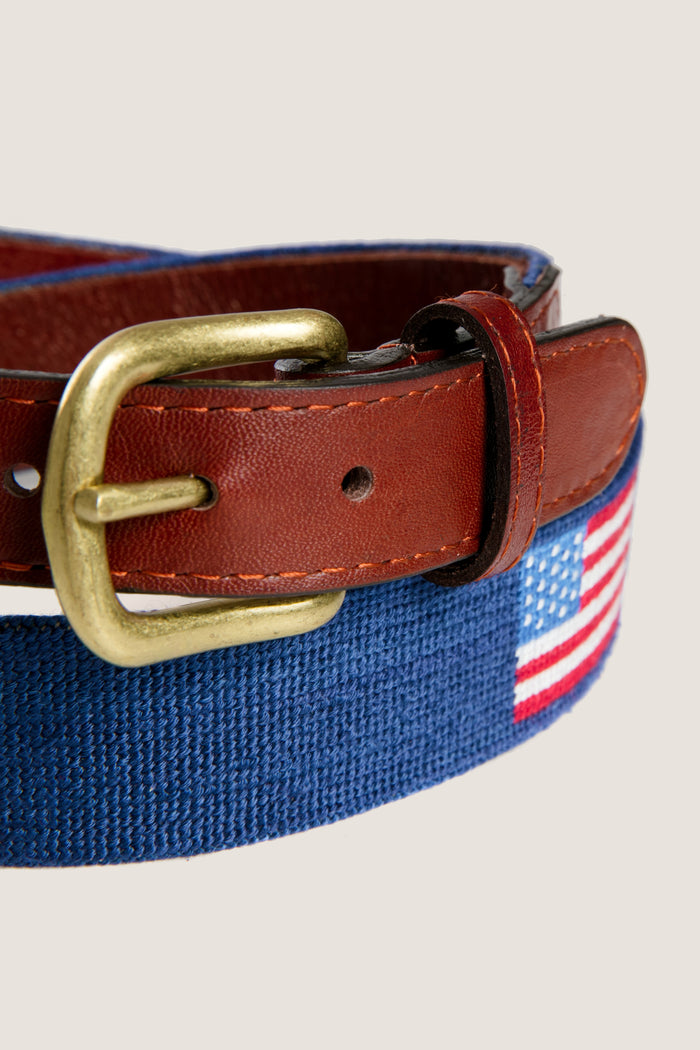 Classic American Flag Needlepoint Belt with blue textile, brown leather trim, and brass buckle. Effortlessly combines fun and high-end style for versatile, patriotic fashion.