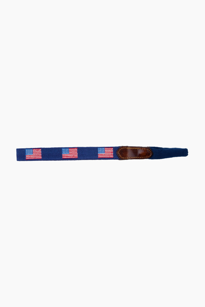 A navy blue fabric belt by Smathers and Branson, featuring hand-stitched American Flag needlepoint designs and a brown leather accent.