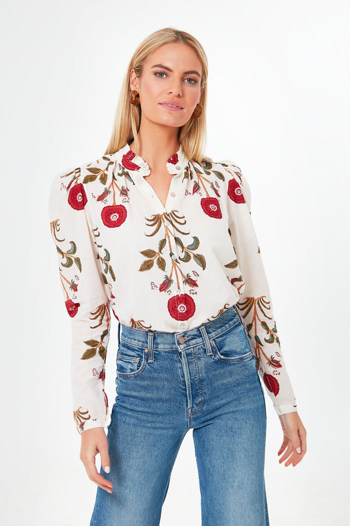 A woman wears an Alix of Bohemia white blouse with red floral print and a ruffled mock neck, styled boho-chic with blue jeans.