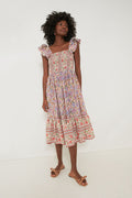 A woman wears the Mille Avignon Floral Olympia Dress, a sleeveless, floral midi dress with ruffled straps and a smocked bodice, paired with bow sandals.
