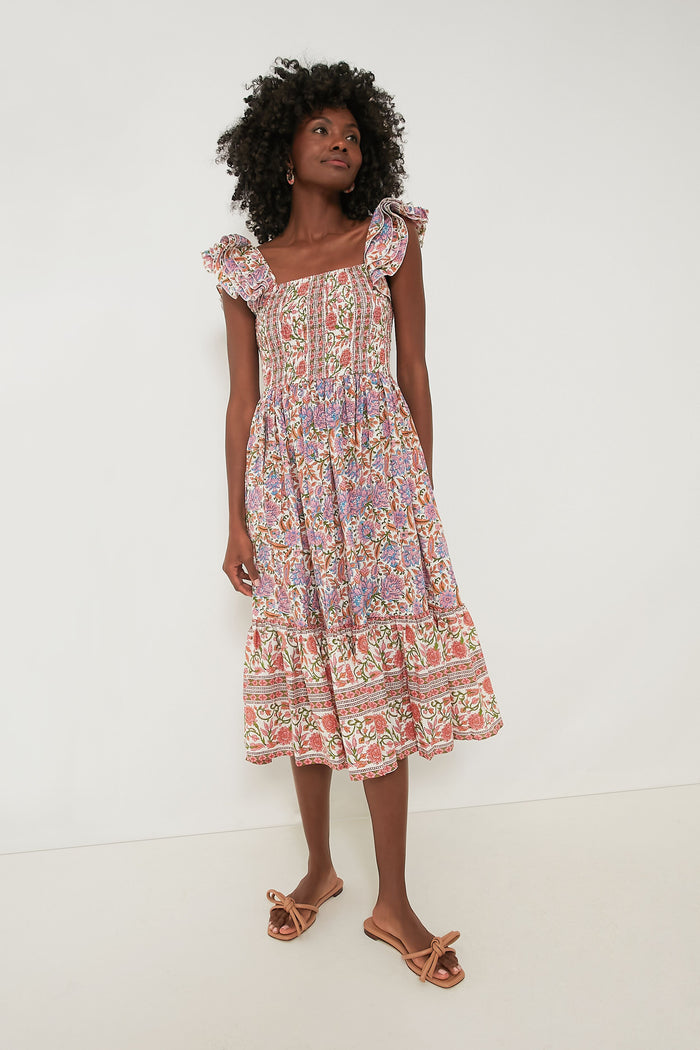 A woman wears the Mille Avignon Floral Olympia Dress, a sleeveless, floral midi dress with ruffled straps and a smocked bodice, paired with bow sandals.