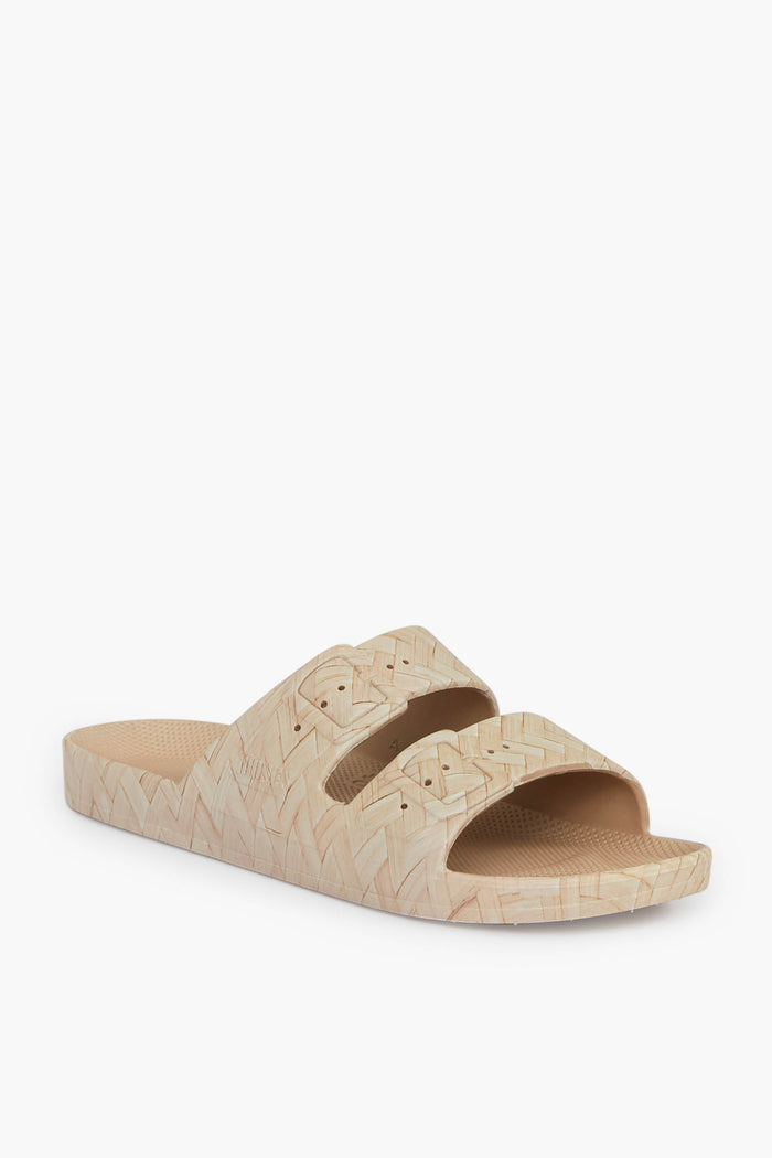 The Freedom Moses beige sandal features two wide straps with a textured, woven pattern on both the straps and sole. This stylish vegan sandal offers a sustainable footwear choice for eco-conscious shoppers.