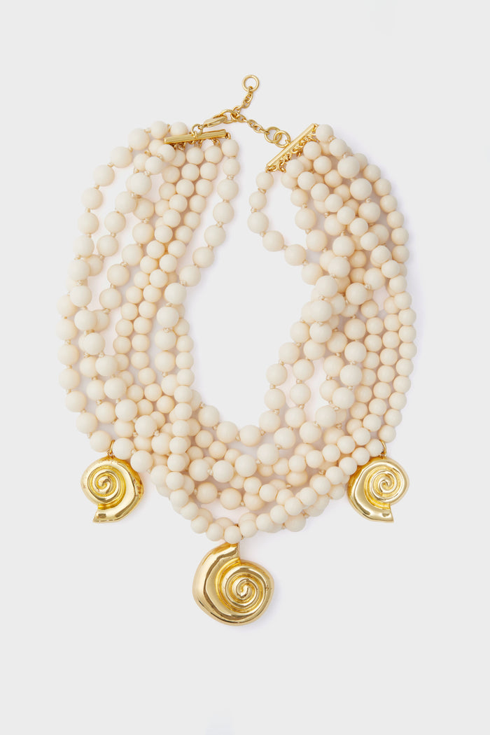 Tuckernuck Jewelry multi-strand cream beaded statement necklace with three gold shell pendants and a gold clasp.