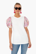 A woman wears Pomander Place sunglasses, a white Bermuda Pink Sorbet top with colorful puff short sleeves, blue jeans, and pink statement earrings.