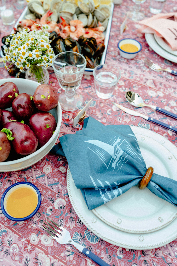 Close up of a summer table setting with a red tablecloth, a blue sailboat napkin, and blue silverware.