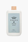 A white Tocca Laundry Delicate bottle with a beige cap and light blue label, ideal for fine fabrics. This gentle detergent cleans while leaving a fresh lemon scent.