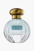 A clear glass bottle of Tocca Bianca perfume with a gold cap and blue label, offering a fresh floral scent accented by hints of green tea.