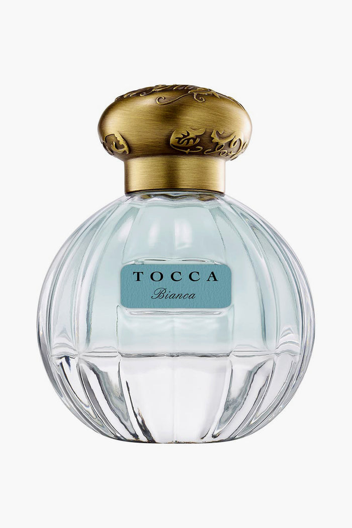A clear glass bottle of Tocca Bianca perfume with a gold cap and blue label, offering a fresh floral scent accented by hints of green tea.