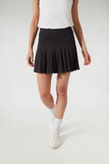 A person in Tnuck Sport’s white sleeveless top, pleated tennis skirt, white socks, and white sneakers stands confidently.