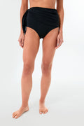 A person stands barefoot wearing Palm Swim's high waist black side tie swimsuit bottom, showcasing sustainable swimwear.