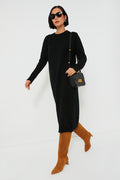 A woman walks confidently in a Tuckernuck black speckled knit maxi dress, brown knee-high boots, a black handbag, and sunglasses.
