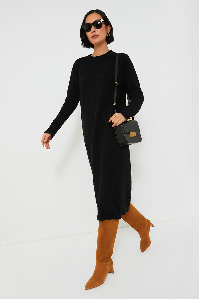 A woman walks confidently in a Tuckernuck black speckled knit maxi dress, brown knee-high boots, a black handbag, and sunglasses.