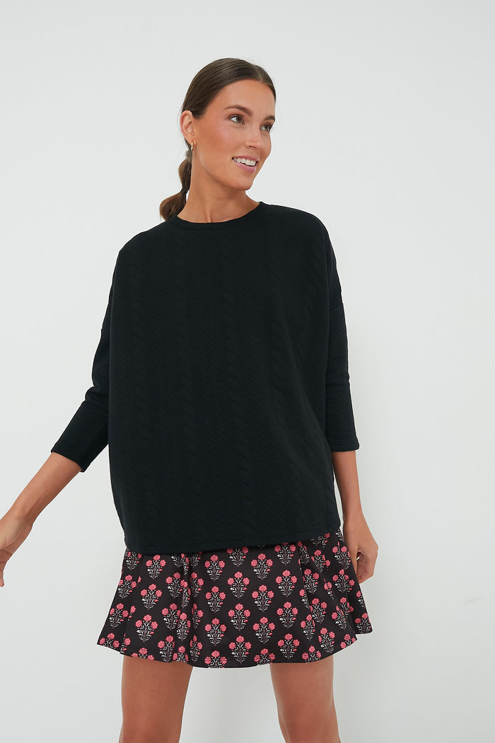 A woman wearing a relaxed fit Tnuck Sport sweatshirt and a short black skirt with a pink floral pattern, looking to the side and smiling.
