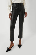 A person wears Veronica Beard black vegan leather kick flare pants, a white button-up shirt, and black heeled shoes with bows.