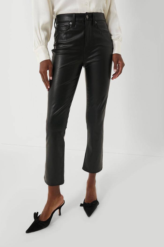 A person wears Veronica Beard black vegan leather kick flare pants, a white button-up shirt, and black heeled shoes with bows.