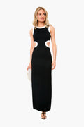 A woman wears the STAUD Dolce Dress, a sleeveless black ponte maxi with white trim and side cutouts, accessorized with a small white clutch.