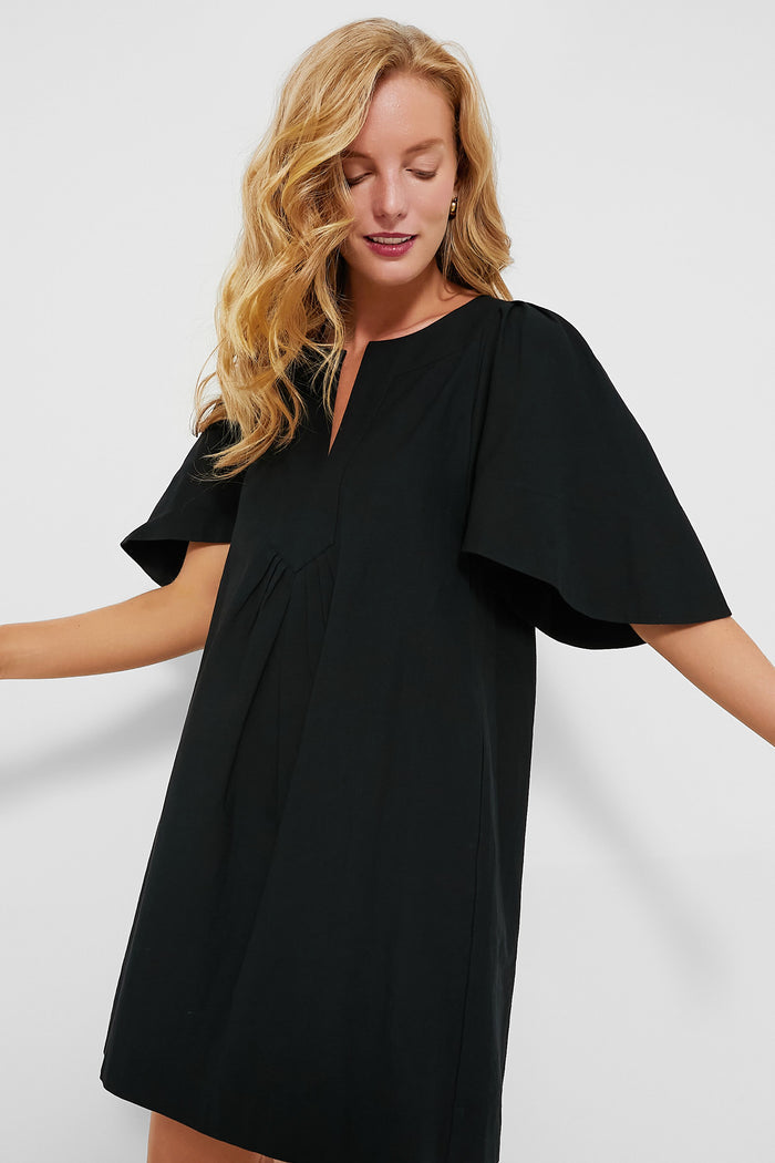 Young woman in a classic, effortless Black Finley Flutter Sleeve Dress with a notched neckline, showcasing flutter sleeves and soft pleats, embodying high-end, fun sophistication.