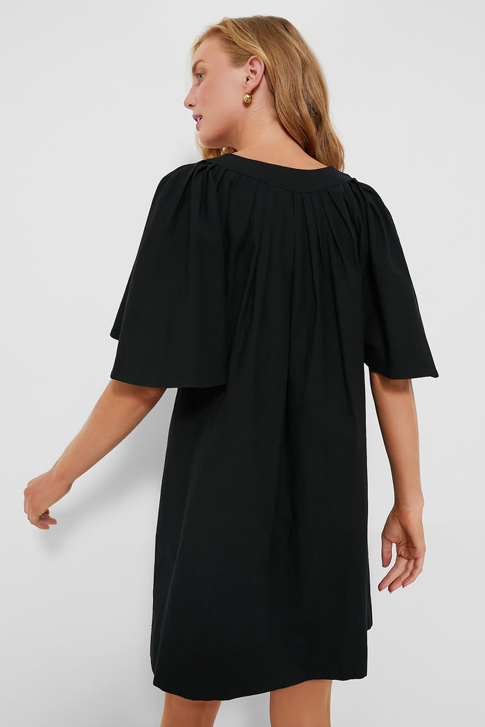 Woman in a classic Black Finley Flutter Sleeve Dress, showcasing effortless style with oversized sleeves and a cape-like drape, embodying Tuckernuck's high-end, fun fashion ethos.