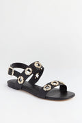 Larroude black leather Milan Sandals feature gold buckle accents, chunky chain strap details, and an ankle strap with buckle closure.