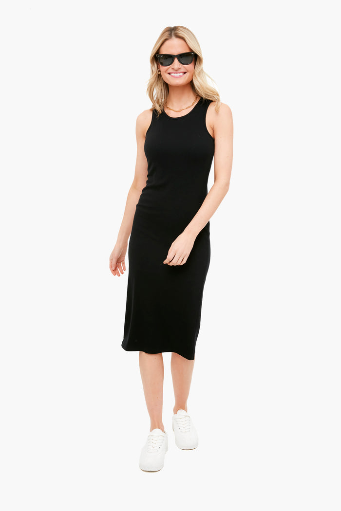 A woman stands smiling in a sleeveless black ribbed midi dress from Marine Layer, paired with white sneakers and sunglasses.