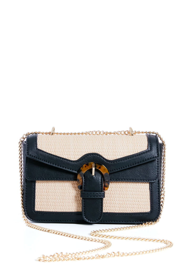 The Moda Luxe bag is a small beige and black vegan leather accessory featuring a gold chain strap and front flap with a tortoiseshell buckle detail.