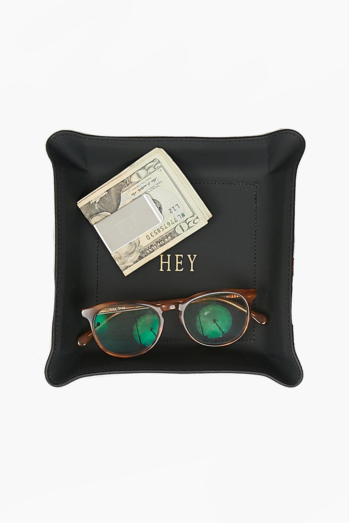 A black leather catchall tray by Graphic Image holds a folded twenty-dollar bill, a credit card, and brown sunglasses with green-tinted lenses.