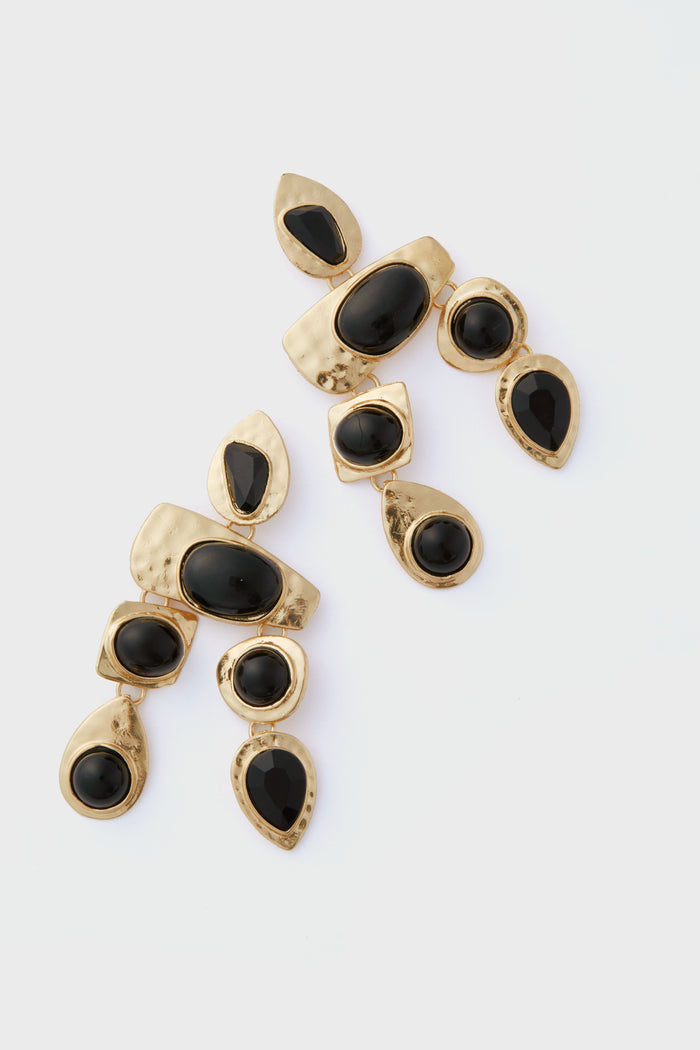 A pair of Petit Moments gold-plated drop earrings featuring multiple black oval and teardrop-shaped resin stones in an abstract design.