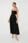 A woman wears a Moon River black dress with scallop trim, thin straps, open sides, minimal jewelry, and beige heeled sandals.