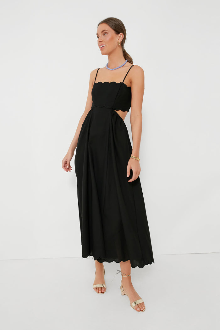 A woman wears a Moon River black dress with scallop trim, thin straps, open sides, minimal jewelry, and beige heeled sandals.