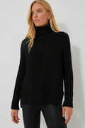 A woman wears a black 525 America Shaker Turtleneck sweater with black leather pants, creating a chic, streamlined look.