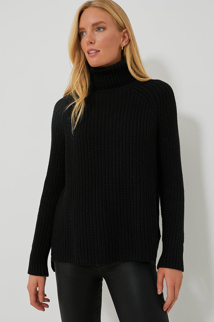 A woman wears a black 525 America Shaker Turtleneck sweater with black leather pants, creating a chic, streamlined look.