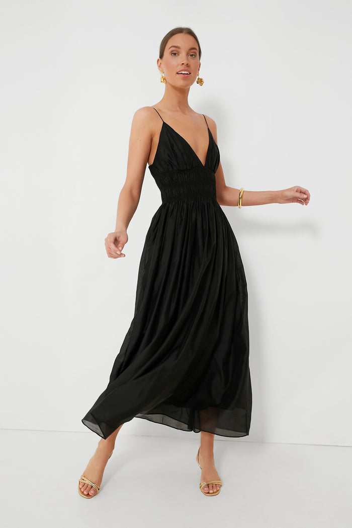 A woman models the Moon River sleeveless black V-neck midi dress with spaghetti straps, paired with gold hoop earrings, a gold bracelet, and beige heeled sandals—an effortlessly chic choice for summer.