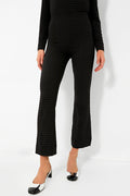 A person wears black textured GANNI pants with a matching long-sleeve top, styled with black and white low-heeled shoes.