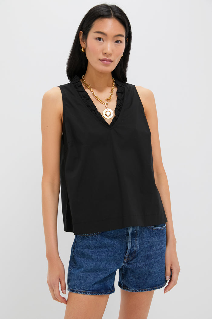 A woman stands confidently in a Pomander Place black ruffle V-neck blouse, gold necklace, and blue denim shorts.