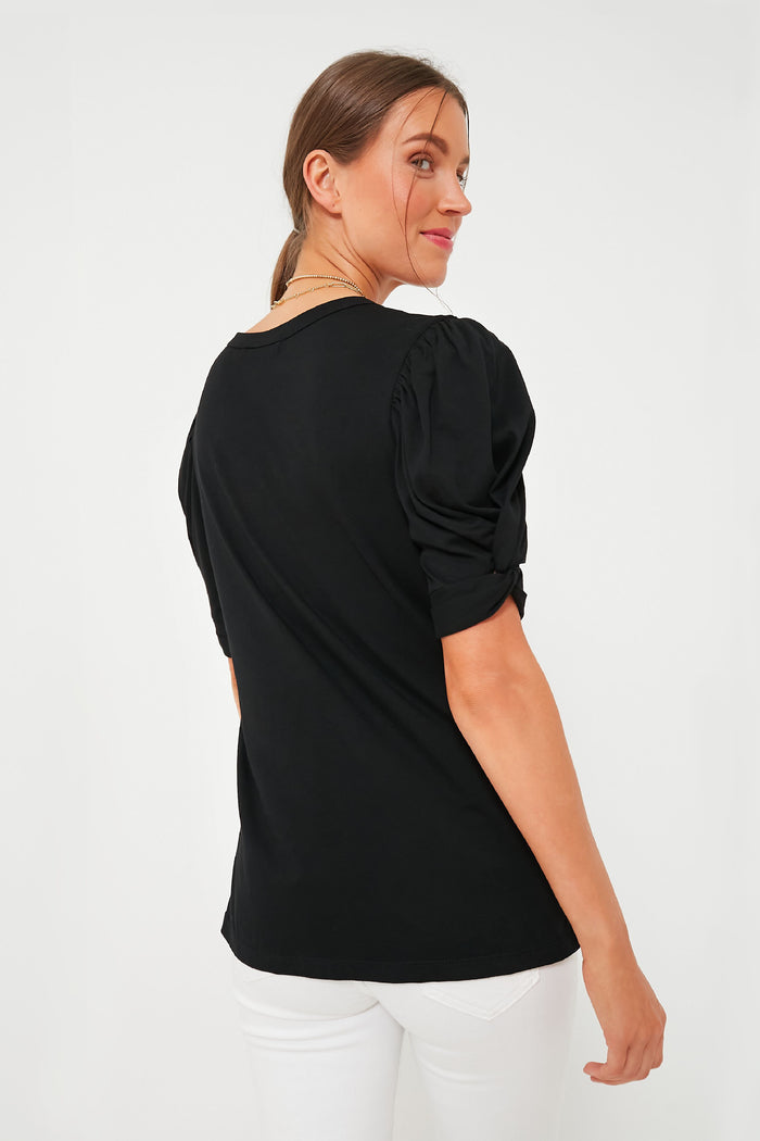 Woman in Black Vesty Puff Short Sleeve Crewneck, featuring classic puff sleeves with knot tie detail, captures an effortless, fun, high-end look paired with white pants.