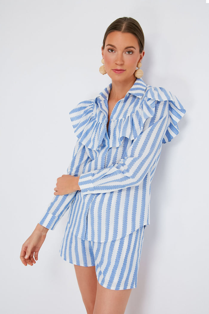 A woman wears a Clare V blue and white striped ruffle detail shirt with scallop stripes, paired with large round earrings.