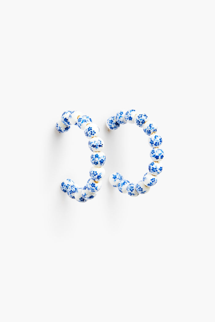 Nicola Bathie Blue Bead Hoop Earrings feature round beads painted with delicate blue flowers, offering a chinoiserie-inspired jewelry style.