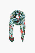 A Tuckernuck Accessories silk Blue Blooming Botanical Scarf, featuring a vibrant floral print in red, green, and blue hues, is styled in a loose knot—an elegant choice for a luxe accessory or those desiring a custom look.