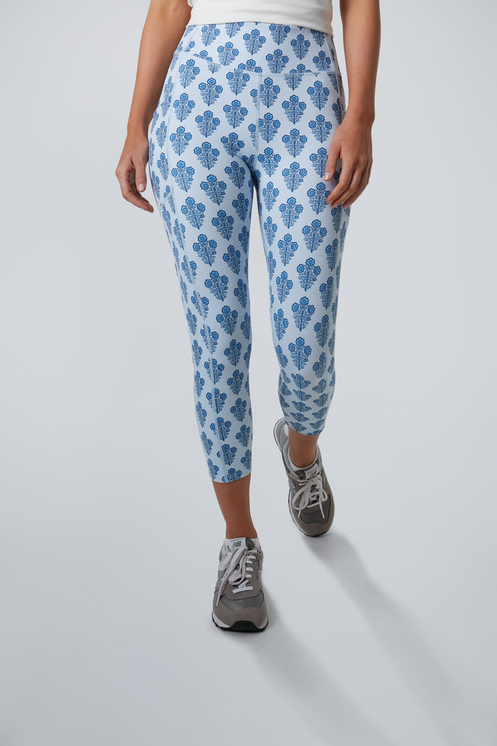 A person wearing Tnuck Sport light blue floral leggings, a Kaylee Capri white top, and gray sneakers stands in a well-lit space.