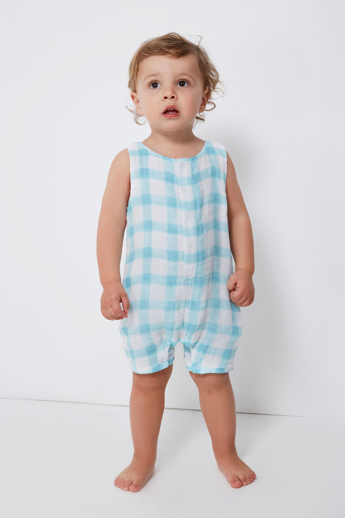 A toddler stands barefoot, dressed in an Angel Dear sleeveless blue and white plaid baby romper crafted from soft organic cotton.