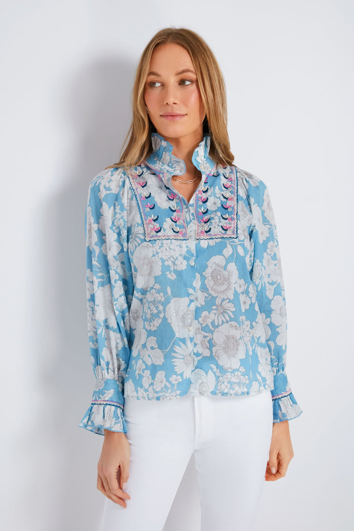 A woman wears an Antik Batik light blue boho blouse with an embroidered yoke and delicate floral details, paired with white pants for a relaxed look.