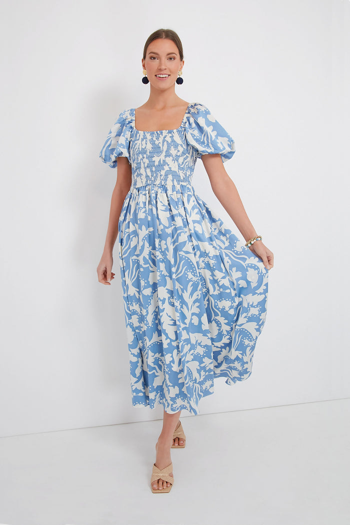 A woman wears a Moon River blue and white floral puff sleeve midi dress with a smocked bodice, paired with beige sandals.