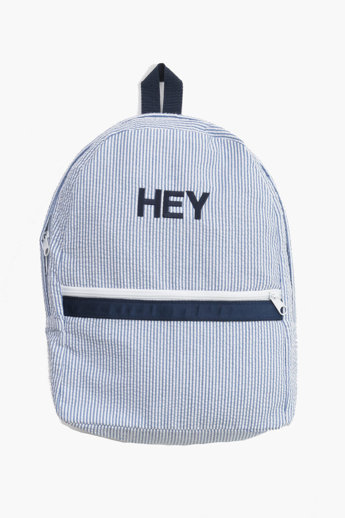 A blue and white seersucker striped Caton's Wharf backpack featuring a front zipper pocket and "HEY" embroidered in black on the front.