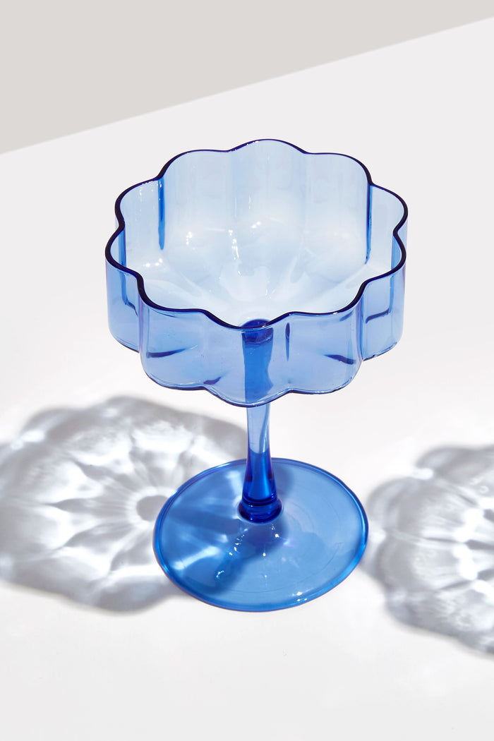 FAZEEK Blue Wave coupe dessert cup with a scalloped edge, made from hand-blown borosilicate glass, rests on a white surface casting delicate light and shadow patterns.